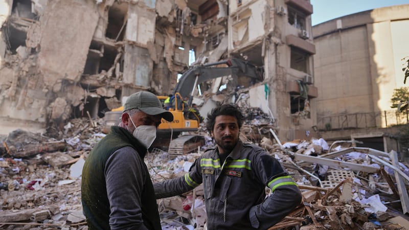 A Lebanese civil defense worker, right, stands with a resident at the site of a building...